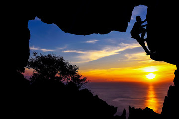 Photographer climbing in the cave on the mountain at sunset 