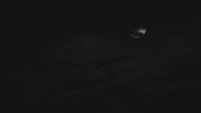 Time lapse clouds with the moon behind them in the night sky. 