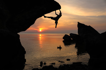 Man climbing the rocks near the sea with purple sky sunset background. 