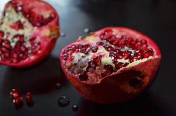 Ripe pomegranate on a black wooden background, juicy pomegranate fractured into pieces, close-up, grain ripe pomegranate