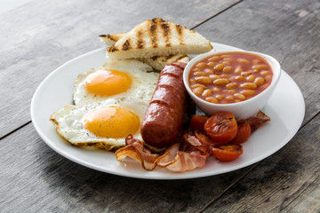 Traditional full English breakfast with fried eggs, sausages, beans, mushrooms, grilled tomatoes and bacon on wooden background
