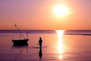 The girl walked on the beach with a fishing boat and sunset.At Nathon Samui Island. 