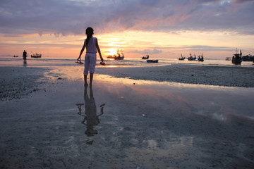 Fototapeta na wymiar Asian girl holding shoes looking sunset on the beach. 