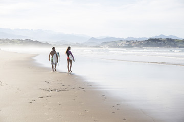 Couple carrying surfboards walking on the beach