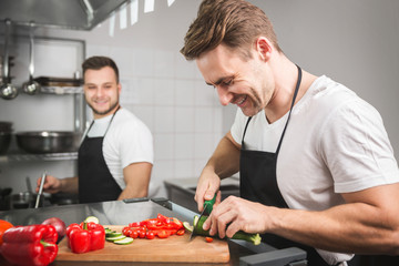 Chef cutting vegetables and his coworker cooking