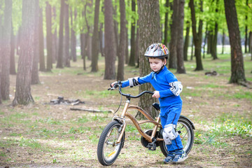 Fototapeta na wymiar Happy cute blond kid boy having fun his first bike on sunny summer day, outdoors. child making sports. Active leisure for children. wear safety helmet. is smiling and cicling.
