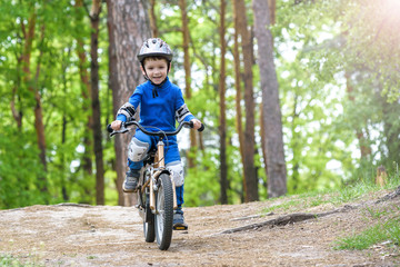 Fototapeta premium Happy funny little kid boy in colorful raincoat riding his first bike on cold day in forest.