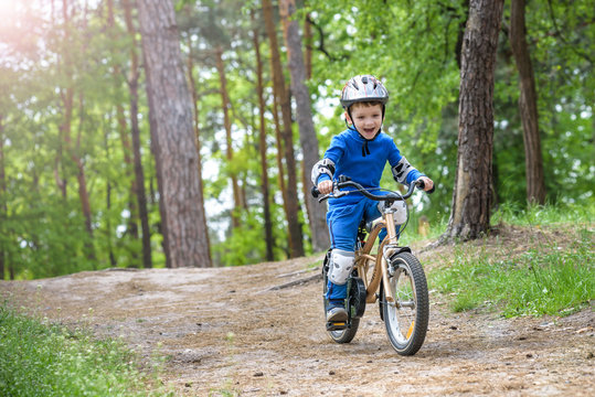 Happy cute blond kid boy having fun his first bike on sunny summer day, outdoors.  child making sports. Active leisure for children.  wear safety helmet.  is smiling and cicling.