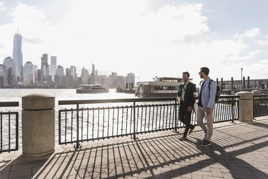 USA, two businessmen walking at New Jersey waterfront with view to Manhattan