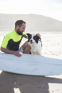 Man with dog putting paraffin on his surfboard on the beach
