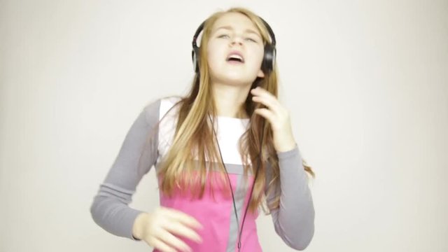 young girl listening music on headphones, singing and funy dancing