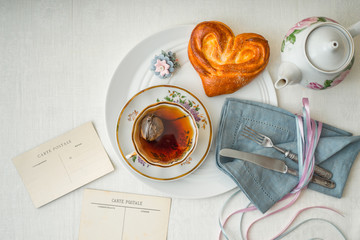 Still life with tea and sweet heart bun on the white table top view