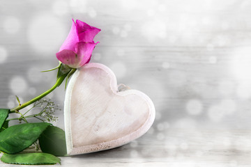 Pink rose and a wooden heart against a light gray bokeh background