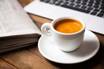Cup of espresso with laptop and newspaper on wooden desk - 132960672