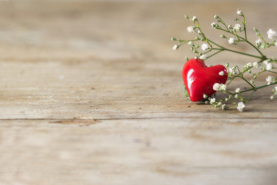 Small red heart from glass and white flowers on a rustic wooden background, copy space