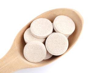 Vitamin pills on a wooden spoon on white background