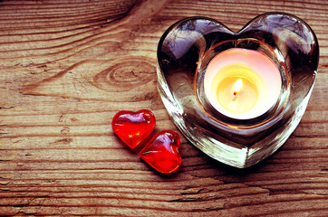 Heart shaped candle holder with burning candle and two decorative red hearts.Saint Valentine's Day or love concept.Vintage filtered.Selective focus.