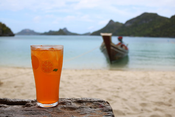 Glass of orange juice and shadow of hand on the beach with views of the archipelago Islands and long-tail boats. 