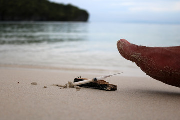 Foot step on injection needles on the beach. 