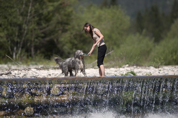 Beautiful woman playing with dog in water. They are standing on top of the waterfall, she is...