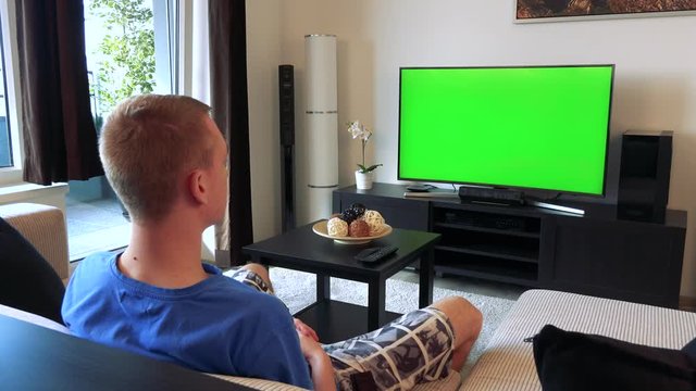 A man watches a TV with a green screen in a cozy living room