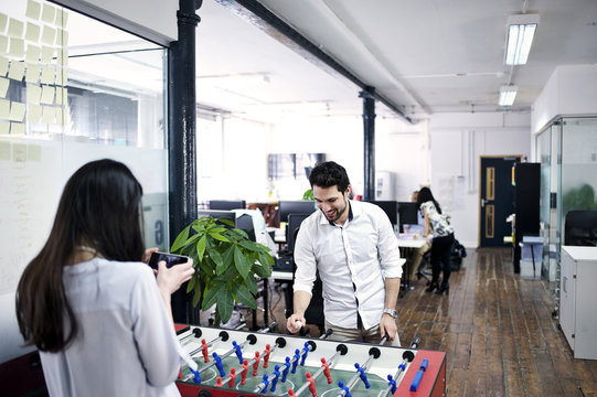 Male and female caucasian office colleagues playing table football in an informal office