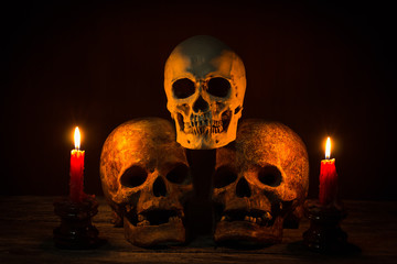 Still life with group of human skulls and candle light on wooden