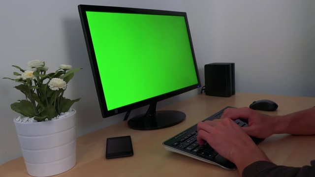 A young, handsome man sleeps with his head on a desk in front of a computer green screen
