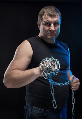Actor Brutal man with a chain in his hands on a black background.