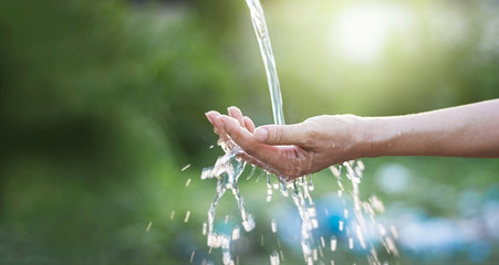 Water pouring in woman hand on nature background, environment concept - Powered by Adobe