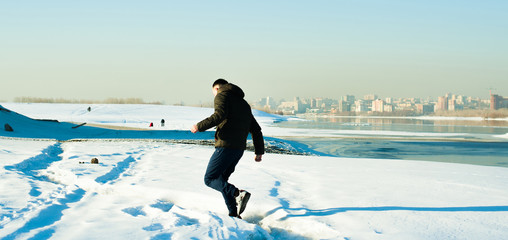 man in warm clothes with a beard is walking on the street in the winter in a warm sunny day at the river against the backdrop of the city