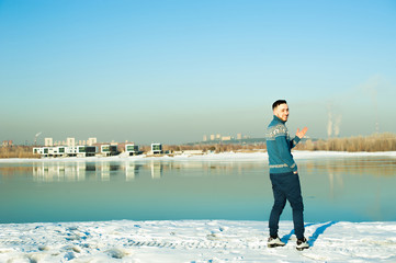 man in warm sweater with a beard is walking on the street in the winter in a warm sunny day at the river against the backdrop of the city, laughing at the problem of the environment and emissions