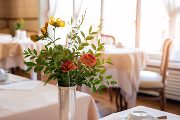 Flowers in vase and sunlight. Interior of food joint. Cozy European restaurant.