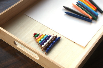 Colored beads on wooden tray with crayons and a piece of paper