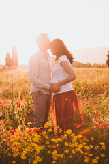 husband kisses his pregnant wife on her front at sunset in field