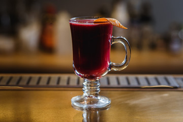 A transparent cup of raspberry mulled wine with orange peel on a bar stand. Selected focus, small depth of field, film grain effect. 