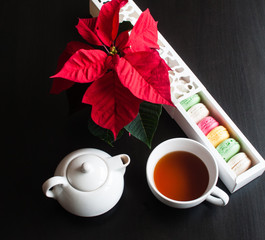 Cup of tea with french macaroon on dark background. Tea pot, cup of tea, color macaroon lying on black background.