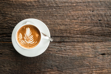 Cup of hot coffee with milk art on the surface placed on the wooden table.