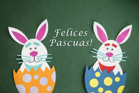 Funny handmade cartoon rabbits placed inside eggs and text in Spanish "Felices Pascuas", which means "Happy Easter holidays", in a green background