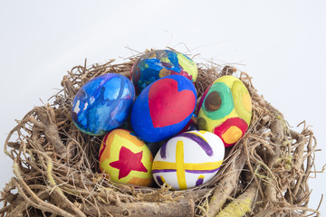Obraz premium Detail of painted Easter eggs placed in a nest with different forms and animals in white isolated background.