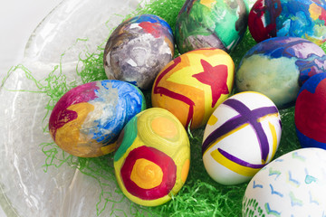 Detail of painted Easter eggs with different forms and colors placed on a glass dish.