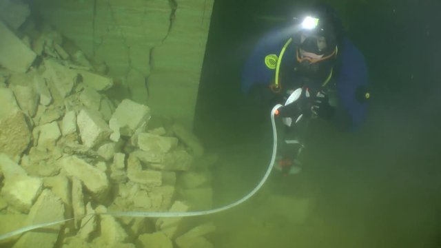 Speleologist swims along the corridor of flooded mine twisting a tape measure.

