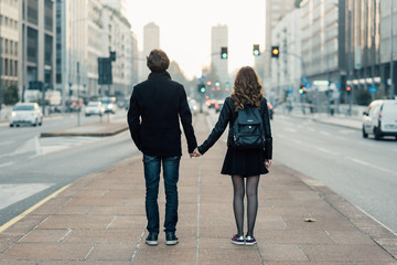 Back view of young beautiful couple in love hand in hand walking outdoor in the city, having fun - first date,  romantic, love concept - obrazy, fototapety, plakaty