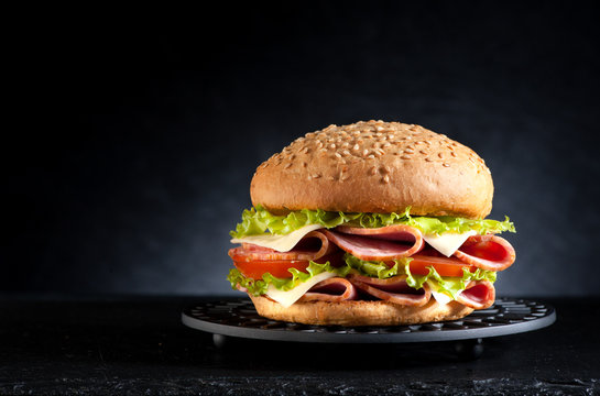 Sandwich Burger with ham cheese and vegetables on a black background.