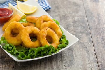 Fried calamari rings with lettuce and ketchup on wooden background
