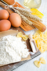 Pasta fusilli, rolling pin, ears of wheat, vegetable oil and eggs on a white wooden background