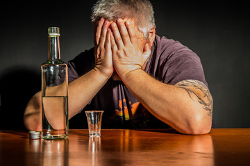 ein Mann sitzt mit einer Flasche Alkohol an einem Tisch - obrazy, fototapety, plakaty