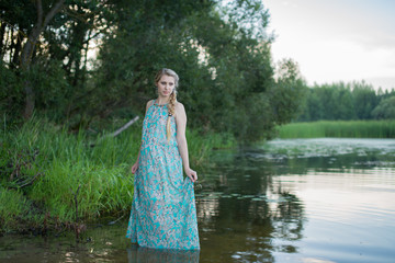 Беременная девушка в платье стоит в реке