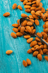 handful of almonds in metal spoon on a blue wooden background
