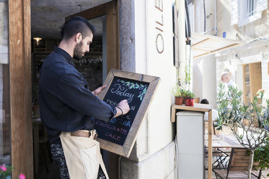 Male owner of oil bar writing menu on blackboard
